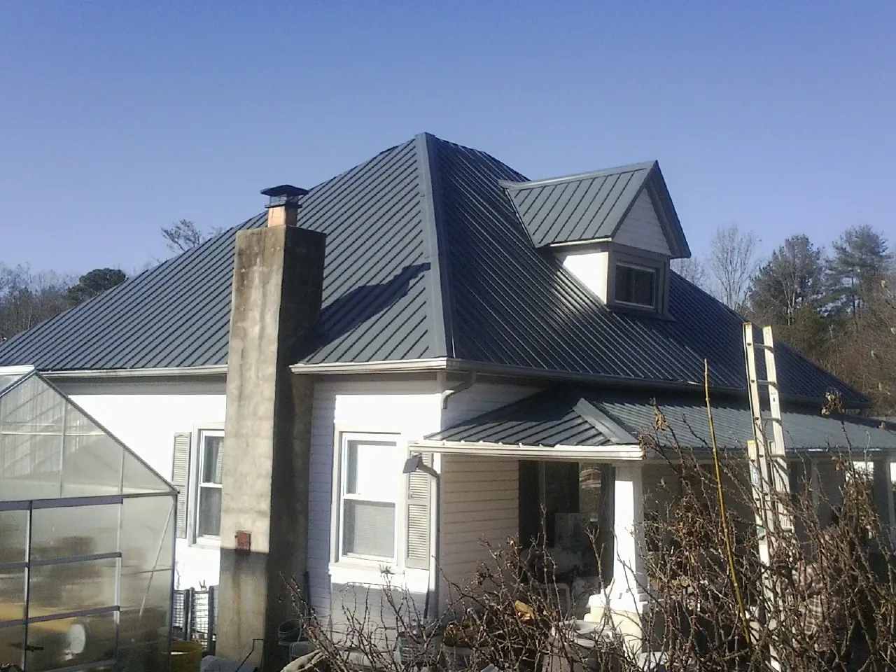 Dark blue standing seam metal roof on a white farmhouse with dormer — Slate & Tile Roof Repair by Roofing Brothers in Babylon