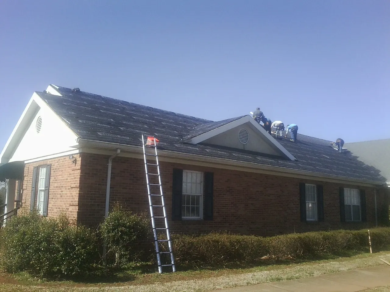 Crew tearing shingles off a brick ranch roof with a ladder set — Metal Roof Repair work by our crew in Babylon