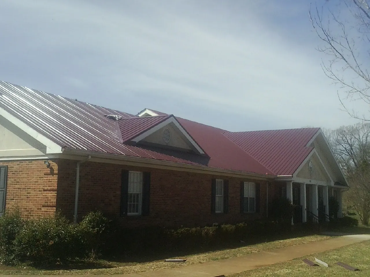 Red metal roof with gabled entries on a long brick building, from a Hail Damage Roof Repair job in Babylon
