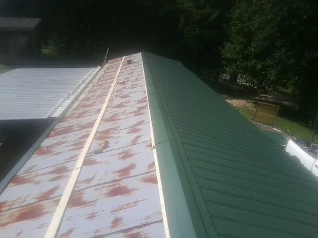Old rusted panels beside newly installed green metal roofing — Wind Damage Roof Repair by Roofing Brothers in Babylon
