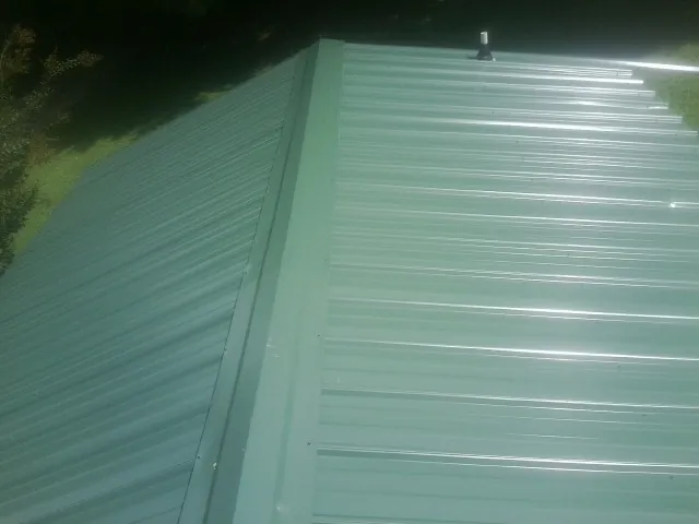 New green metal panels meeting at the ridge of a roof — Flat Roof Repair work by our crew in Babylon