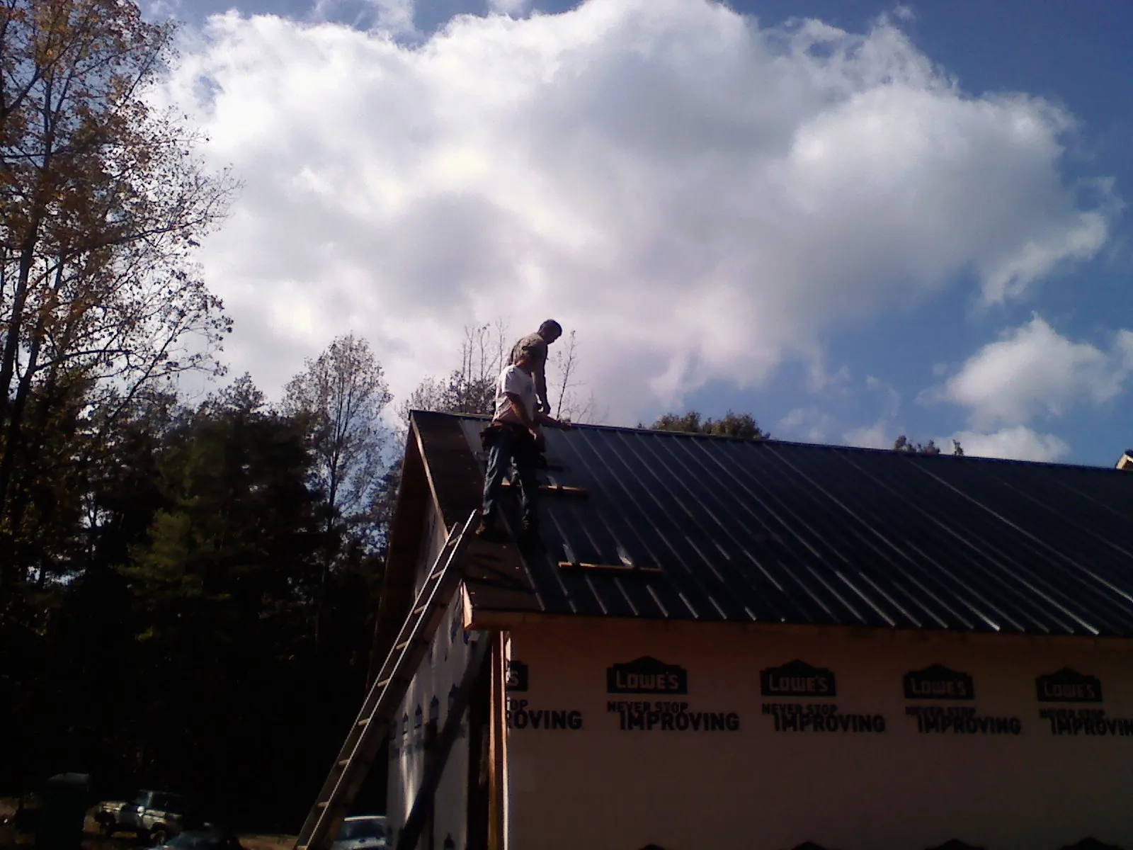 Roofer fastening dark metal panels high against a cloudy sky, from a Roof Inspection job in Babylon